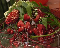 Assemblage de roses bicolores et euphorbe fleurs blanche dans une boule de petits cœurs le tout fixés par des mikados rouges dans une coupe sur pied en verre